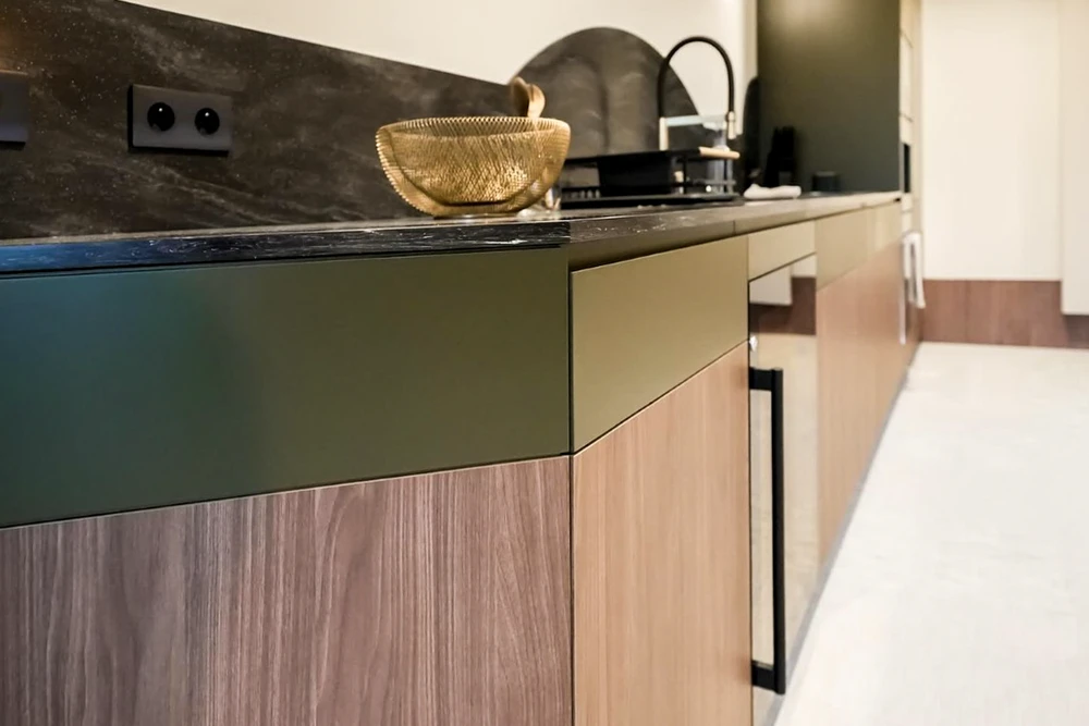 Cuisine moderne avec îlot central, plan de travail en pierre naturelle veinée sombre, façades en bois clair et laque verte olive
