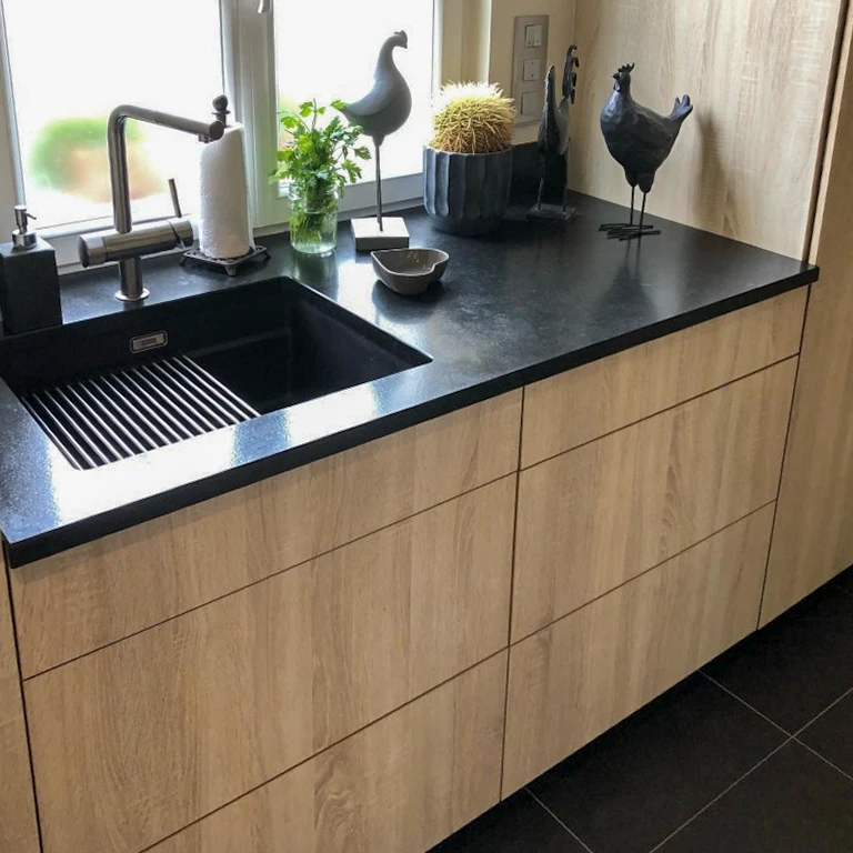 Cuisine moderne avec plan de travail noir en pierre naturelle, façades en bois clair, évier noir intégré avec égouttoir rainuré