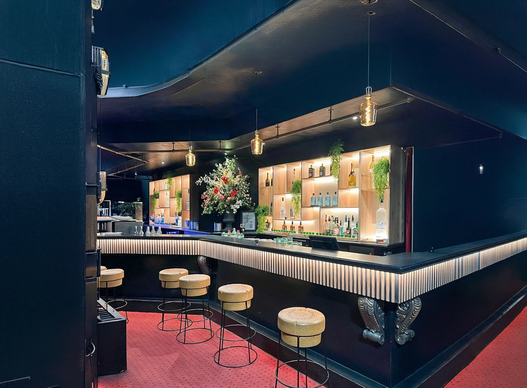 Trois hommes assis autour d'une table de bar en bois foncé dans un pub, tenant des chopes de bière blonde